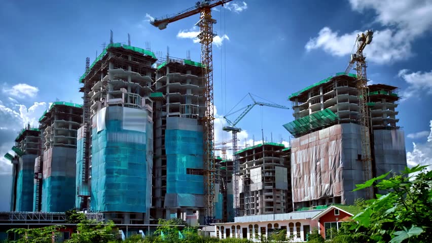 time lapse Tall buildings under construction reach towards bright blue sky with white clouds. Cranes are building multiple high rise structures. Located in Asia, construction booms.