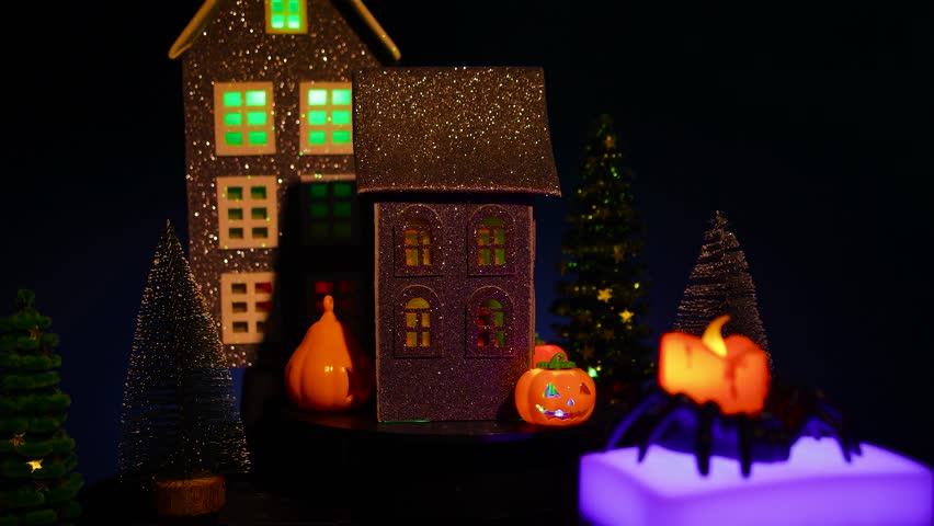 Against the backdrop of a house with Christmas trees and a Halloween black house with lights in the windows, surrounded by glowing candles and pumpkins, a candle moves in a spider candlestick