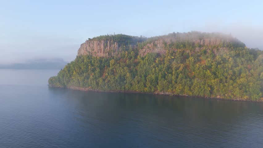 Fog rolls across the wild Ontario coast of Lake Superior, shrouding steep cliffs and golden autumn trees in a quiet, ethereal light.