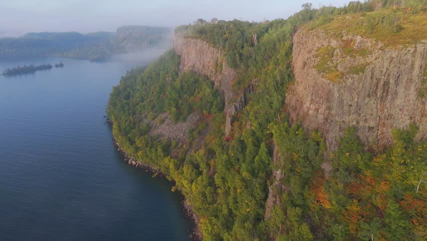 calm waters of Lake Superior reflect steep cliffs and vibrant fall colors from the surrounding Ontario forest