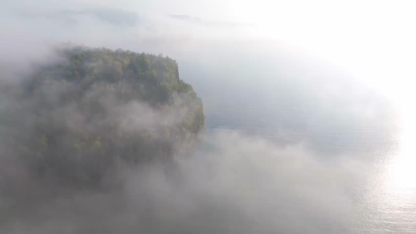 Dense fog Vertical cliff and forest during early autumn at Lake Superior shoreline in Ontario, Canada.