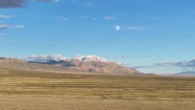 Aerial view of snow-capped mountains with moon visible in blue sky over vast uninhabited grassland plateau in remote wilderness area - Powered by Shutterstock - Get 15% off with code: PIKWIZARD15
