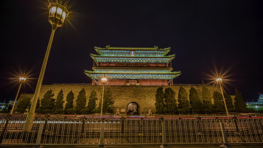 Night view of illuminated Zhengyangmen Gate in Beijing, China. Traditional Chinese architecture with colorful lighting and street lamps creating a dramatic cityscape scene.