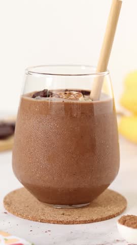 Mixing chocolate smoothie with a straw. Vertical video. Healthy blended breakfast drink. Close-up.