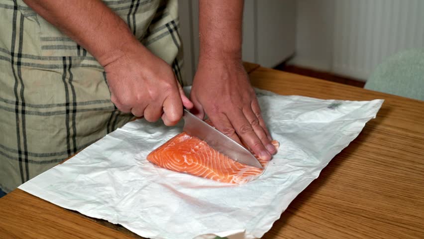 Male hands cutting fresh red salmon on a kitchen board. Fish preparation, healthy food, seafood, cooking process, close-up, fresh ingredients.