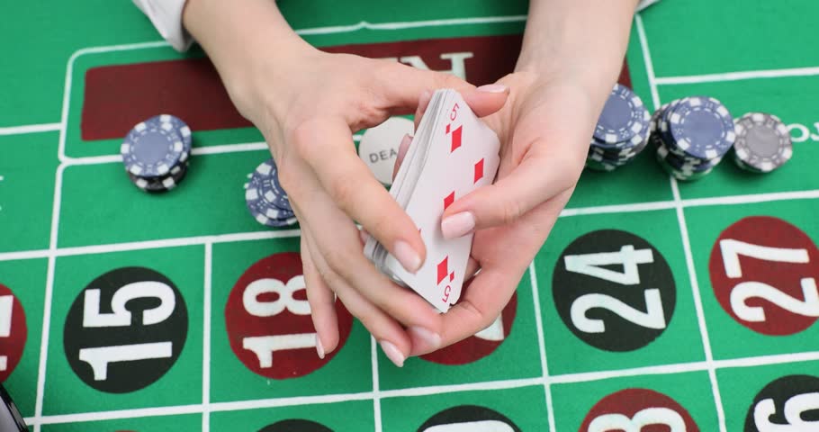 Casino croupier shuffles deck holding two cards above layout. Dealer stacks chips preparing bet and fans pack with quick skilled hands slow motion