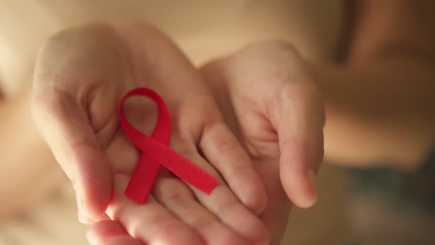 Female hands carefully unveiling red awareness ribbon on open palm, representing solidarity with HIV-positive individuals and December awareness month.