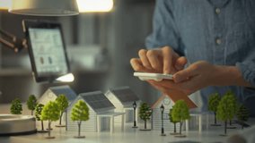 An engineer designer performs calculations on an office calculator against the backdrop of models of private homes designed with sustainable green energy in the form of solar panels. Modern homes - Powered by Shutterstock - Get 15% off with code: PIKWIZARD15