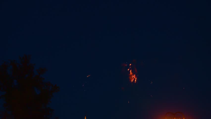 Bright fireworks burst in vibrant colors against the dark sky above a city park, creating a festive atmosphere as spectators enjoy the display during a local celebration.
