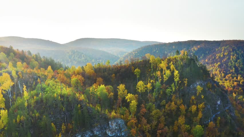 aerial view of vibrant autumn foliage covering the rolling hills and mountains of the South Ural region in the Republic of Bashkortostan, Russia. Golden, orange, and green trees create a stunning natu