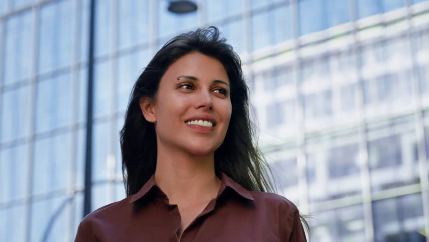 Thoughtful confident proud beautiful woman entrepreneur smiling on skyscrapers city background, feeling freedom. Portrait of Latin successful businesswoman standing outdoor looking dreaming aside. 