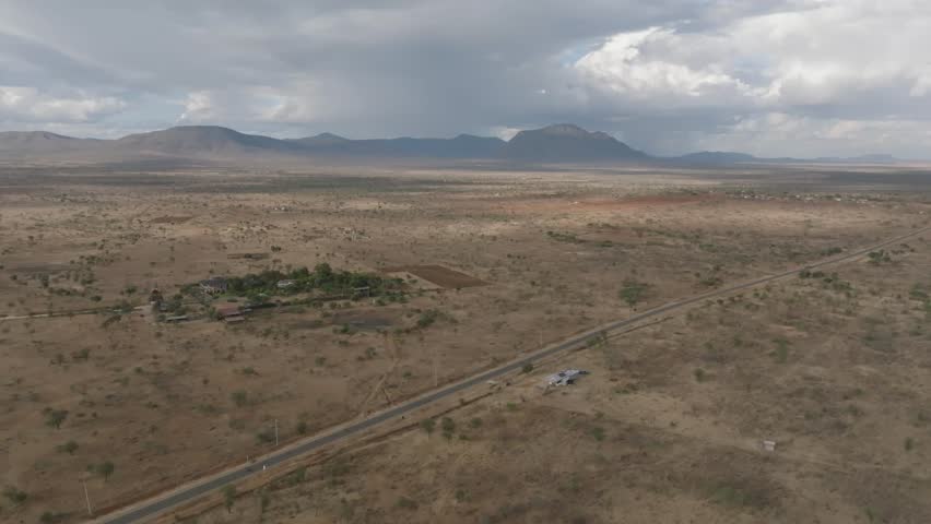 Aerial view of arid landscape featuring a road cutting through sparse vegetation, hinting at life in the distance, Kajiado, Kajiado, Kenya.