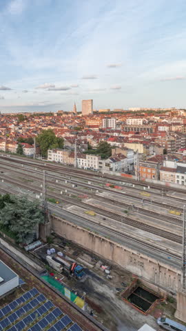 Aerial timelapse of Brussels North station railway tracks with trains arriving and departing. Schaerbeek evening cityscape panorama featuring red rooftops, industrial areas and a cloudy sky. Belgium