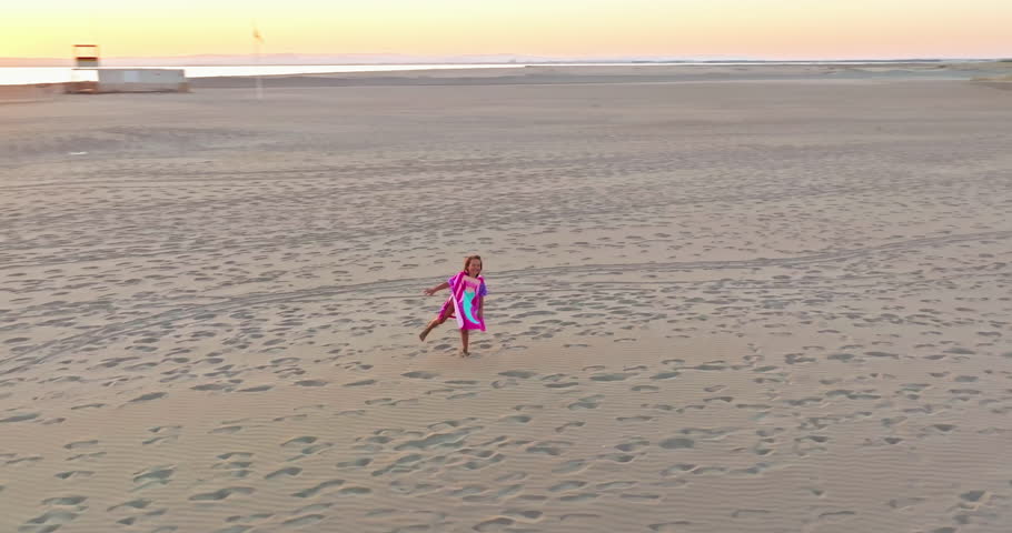 Aerial view of happy playful little girl runs barefoot on the sand beach