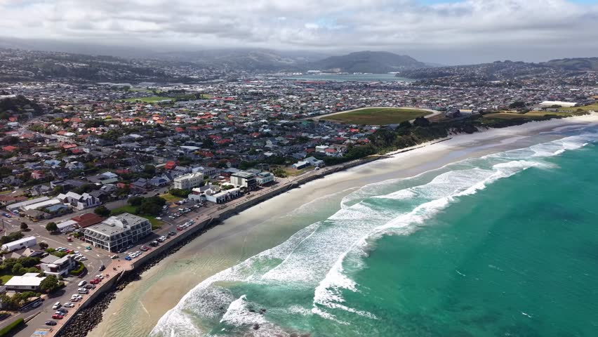 The stunning seaside city of Dunedin located on the coastline of New Zealand's south island displaying a gorgeous seascape of the pacific ocean with white crashing waves, sandy beaches and blue skies