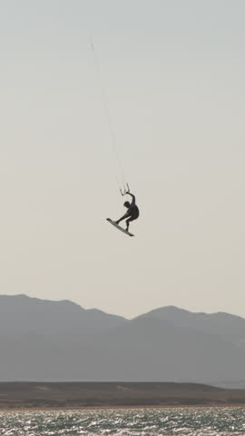 Slow motion vertical video kitesurfer performing megaloop jump at sunset over ocean waves extreme sport lifestyle freedom adrenaline cinematic epic action summer travel nature mountains beach
