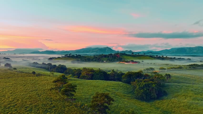 A calm view of fog floating over a green mountain valley in the Dominican Republic. Meadows in the morning light. A colorful sunrise on a foggy, wooded mountainside. Natural beauty of the landscape.