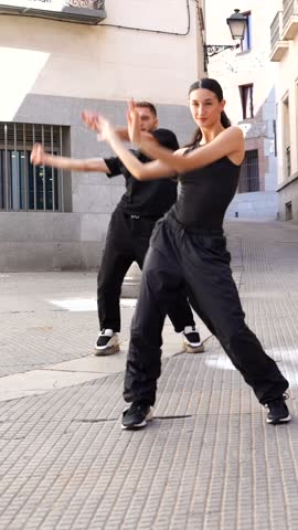 Talented group of young dancers in black clothing performing an energetic and synchronized contemporary dance routine in a narrow european street, showcasing their passion and modern art form