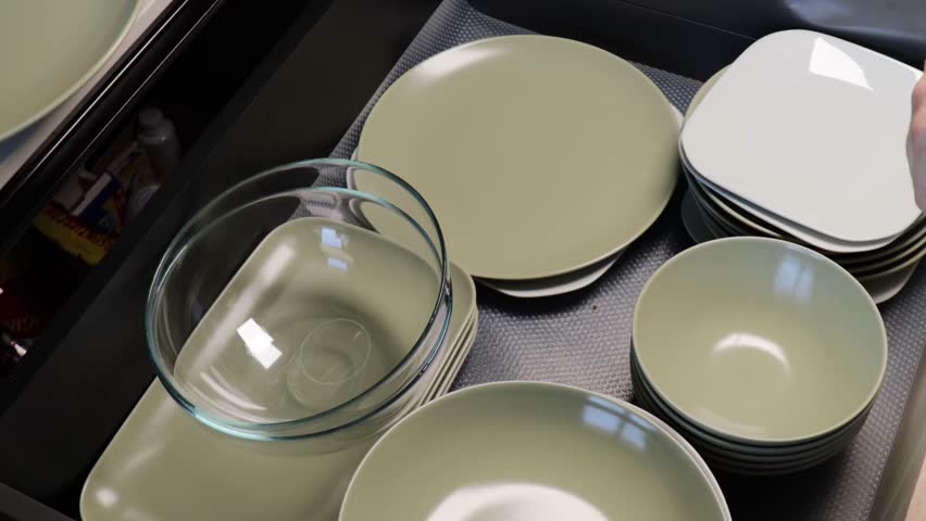 organizing clean dishes on kitchen shelf, hands arranging plates and bowls after washing in modern interior, concept of home organization, cleanliness, kitchen routine, household management industry
