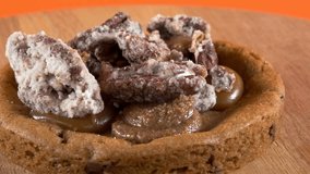 Close-up of a delicious cookie topped with caramel, cream, and sugared pecan, displayed on a rotating wooden plate with an orange background. - Powered by Shutterstock - Get 15% off with code: PIKWIZARD15