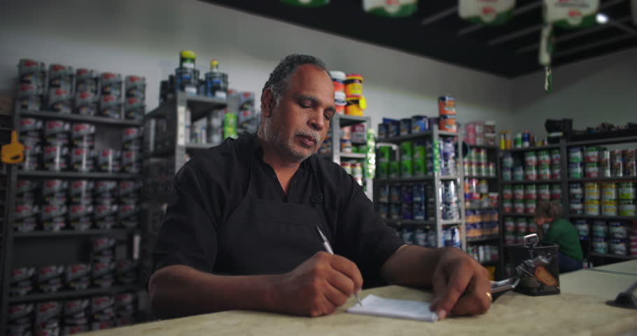 Male shop owner holding his head in frustration, overwhelmed by challenges, contemplating solutions, small business struggles in retail store environment