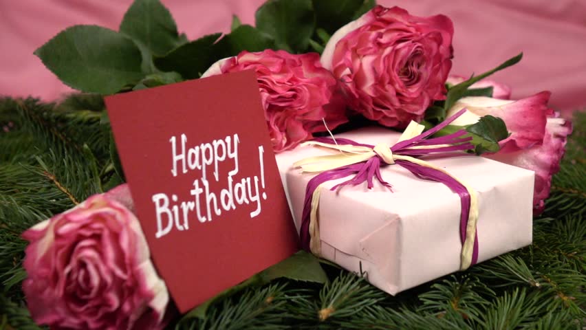 Fresh pink roses, box with present and a card with words " Happy Birthday" on the fir twigs. Festive arrangement, slow motion
