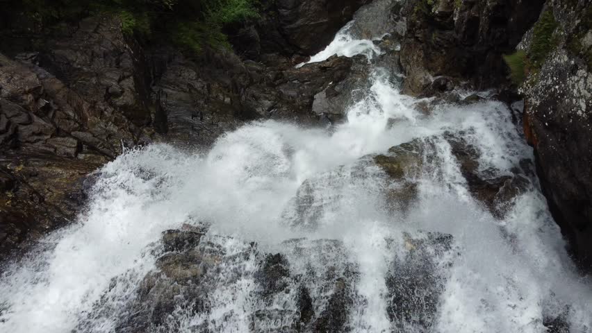 A Scenic view of a powerful mountain waterfall rushing over dark rocks with white foamy splashes