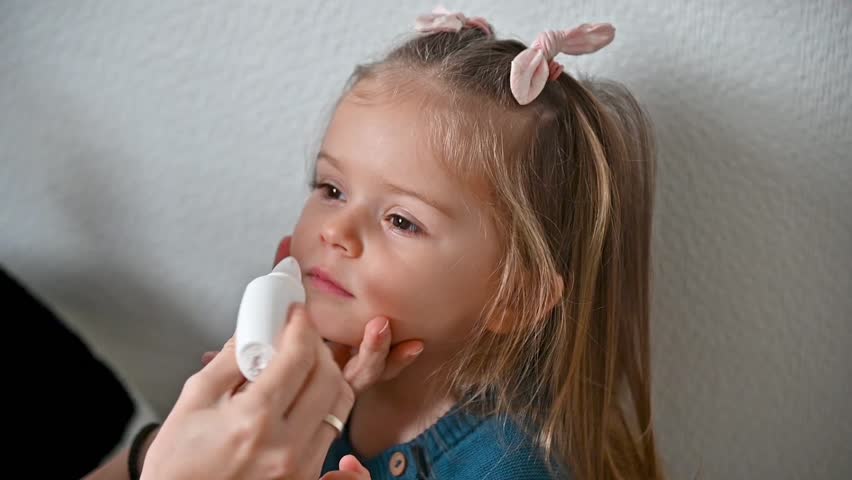 Mother using nasal aspirator also known as snot sucker for her cute toddler girl at home. Full HD slow motion video footage