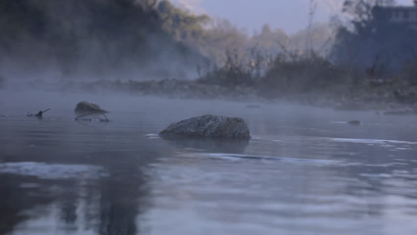 Mist ascends from a gentle mountain river in india surrounded by a rustic landscape of trees and hills during the quiet morning hours, capturing the tranquility of nature bathed in soft winter light.