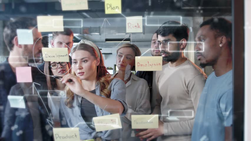 Diverse team of professionals brainstorming around glass board with sticky notes labeled plan, analysis, and product. Holographic diagrams and digital interface overlays showing strategy visualization - Powered by Shutterstock - Get 15% off with code: PIKWIZARD15