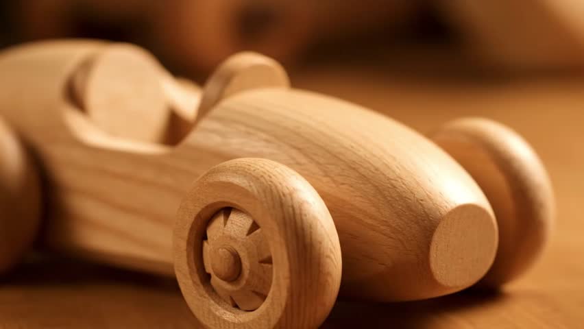 A close-up, shallow depth of field shot of a simple, handmade wooden toy race car. The natural wood grain is visible, 