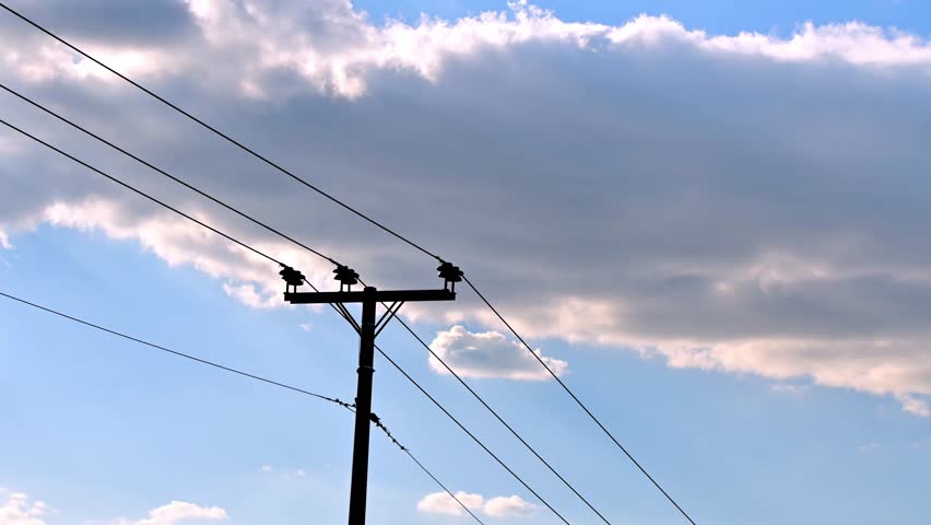 Time lapse footage shows dark clouds passing by at the blue sky behind an electric pillar.