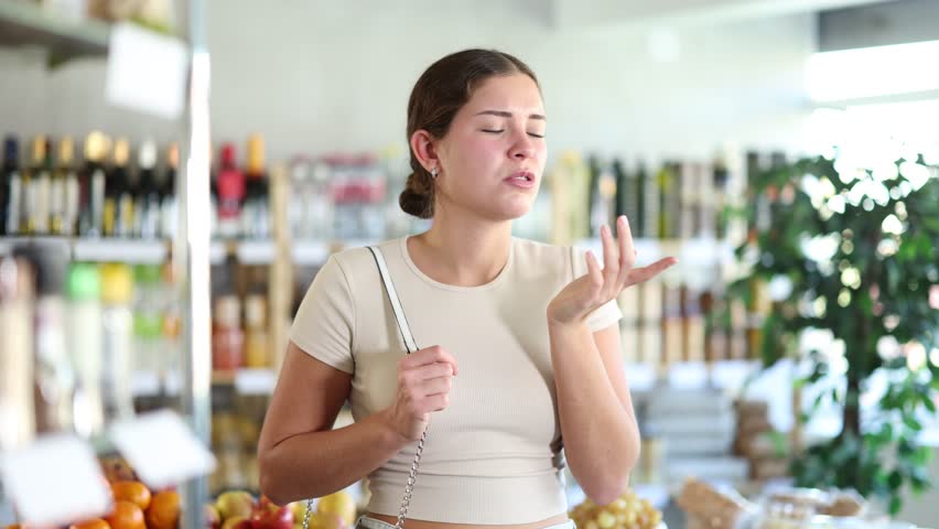 Girl customer suffers from forgetfulness, stands in store and tries to remember planned shopping list. She rubs her forehead, remembers forgotten purchase item