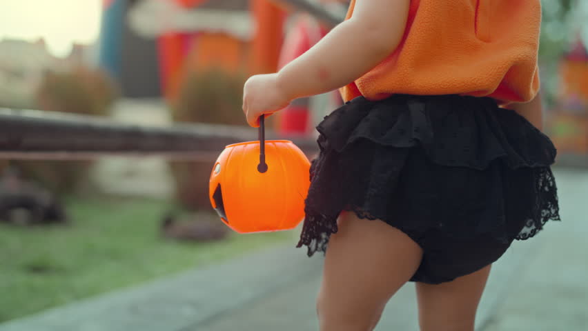 B roll - Close up of little child holding orange jack o lantern bucket during Halloween festival, kid wearing pumpkin costume outdoors, autumn holiday celebration concept with festive atmosphere