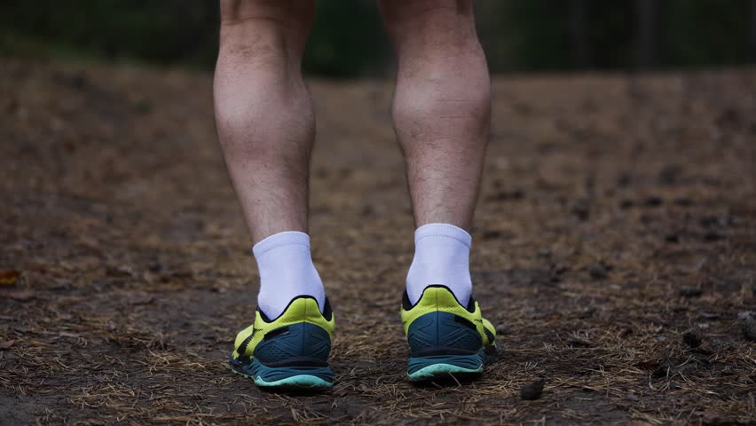Muscular man's legs jumping in place during an intense cardiovascular workout outdoors on a forest trail. Close up of the athlete's feet wearing sneakers and his calves flexing