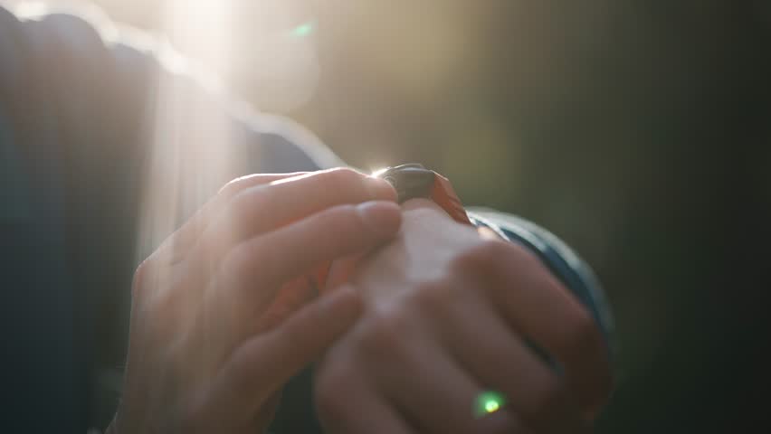 Closeup of a male athlete's hands using a smartwatch to track performance and heart rate during training in a park, with beautiful sunlight creating a lens flare in the background