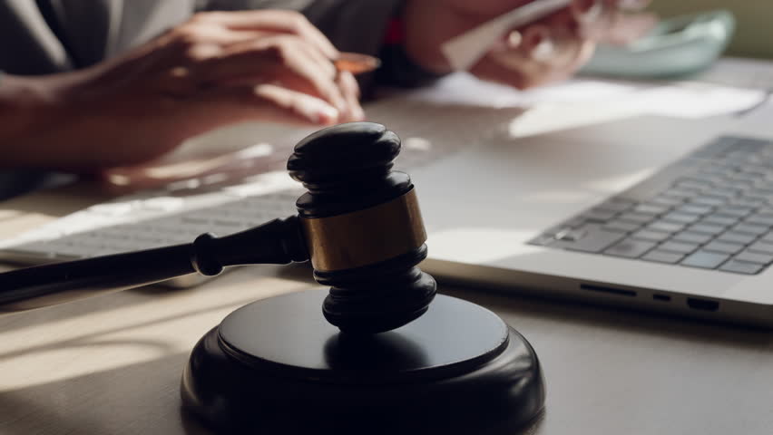 Close up of lawyer hand with pen near gavel and laptop in office. Concept of legal consulting, contract, and digital law service.