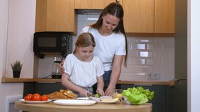 Mom carefully slices cucumber while preparing sandwiches with her daughter, demonstrating cooking skills and enjoying quality family time in their modern kitchen - Powered by Shutterstock - Get 15% off with code: PIKWIZARD15