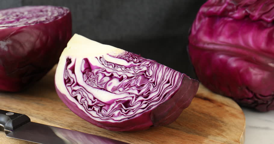 Woman cutting fresh red cabbage at table, closeup