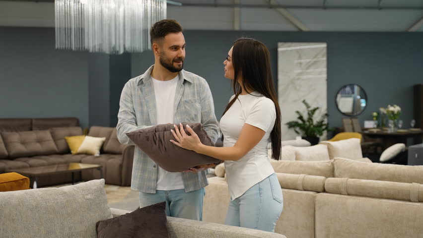 Young couple choosing decorative pillow in furniture store