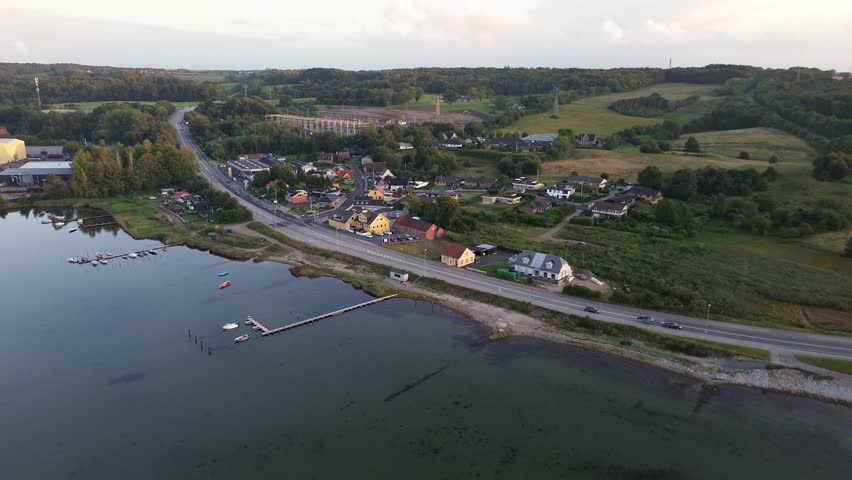 Aerial view of Styrtom near Aabenraa, Denmark. Coastal village with houses, road, marina, and rolling hills in warm evening light