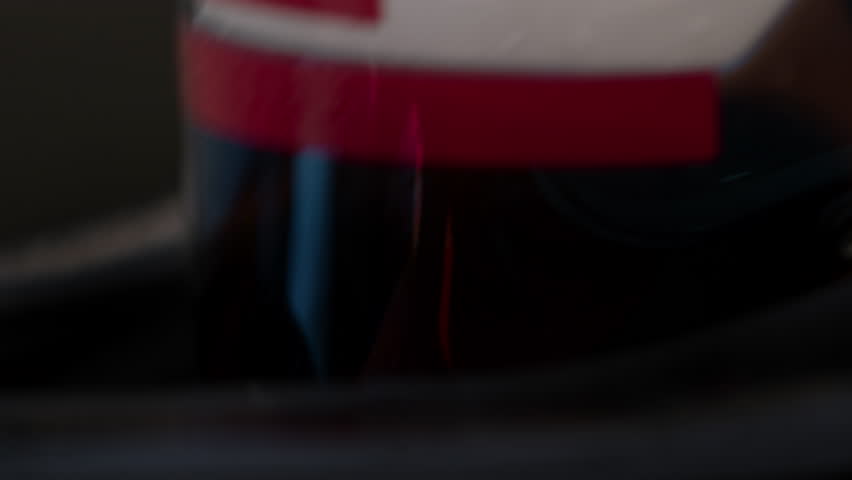 Close-up of a race car driver in a white helmet with red details, driving fast on a racing track, evening race