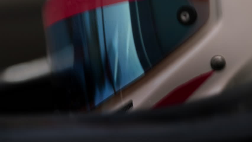 Close-up of a race car driver in a white helmet with red details, driving fast on a racing track, evening race
