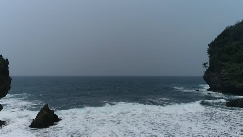 Footage of Srakung Beach in Indonesia, featuring cliffs, greenery, and ocean waves. Ideal for travel, nature, and coastal projects.
