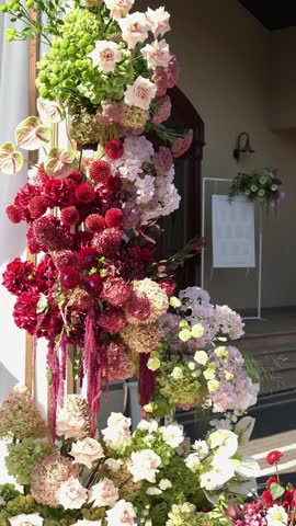 Colorful wedding romantic flower arch with white fabric. Summer atmosphere on the street. Green white and red flowers. Rose, hydrangea, anthurium, dahlia, chrysanthemum, amaranth, dianthus white spray