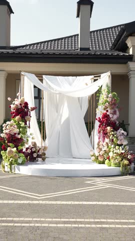 Colorful wedding romantic flower arch with white fabric. Summer atmosphere on the street. Green white and red flowers. Rose, hydrangea, anthurium, dahlia, chrysanthemum, amaranth, dianthus white spray