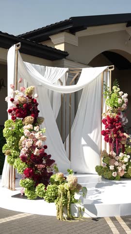 Colorful wedding romantic flower arch with white fabric. Summer atmosphere on the street. Green white and red flowers. Rose, hydrangea, anthurium, dahlia, chrysanthemum, amaranth, dianthus white spray