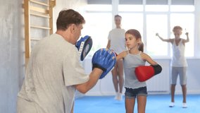 Concentrated sporty tween girl in boxing gloves practicing self-defense techniques with family in gym, throwing punches on focus mitts in hands of father - Powered by Shutterstock - Get 15% off with code: PIKWIZARD15