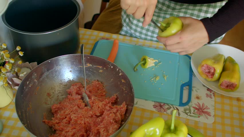 On a kitchen countertop, I am preparing vibrant peppers to be stuffed with a delicious ground meat mixture, with various utensils and fresh ingredients neatly visible around me