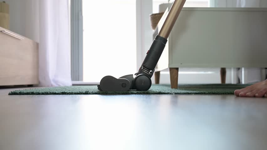Person vacuuming the floor with a cordless vacuum cleaner